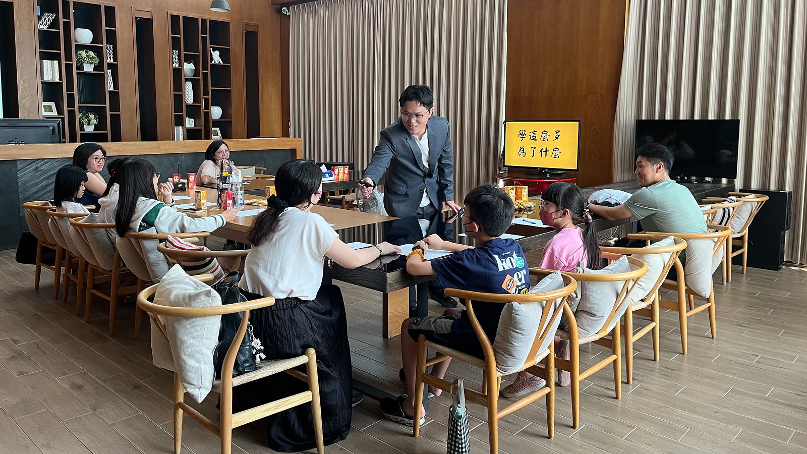 強腦力高雄實體課現場：講師帶著家長與孩子圍著長桌上課，螢幕上寫著「學這麼多 為了什麼」
